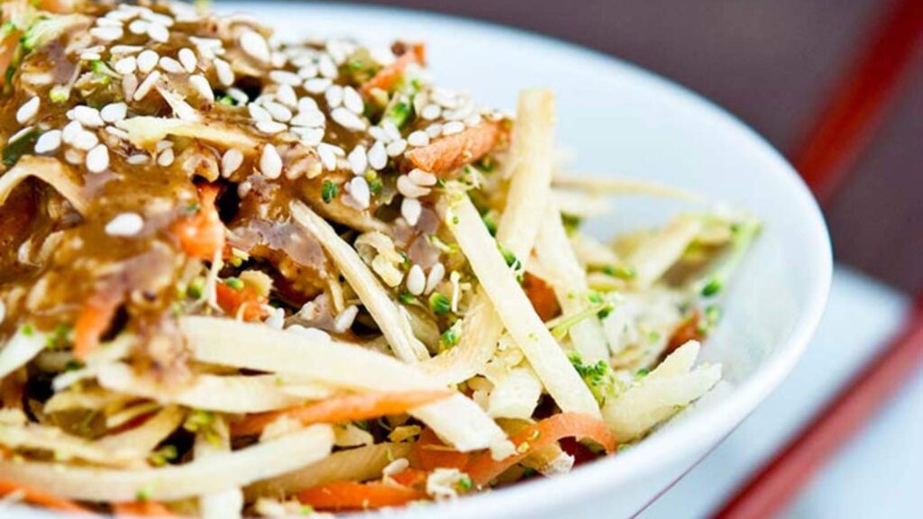 A closeup of a white bowl filled with Asian Raw Broccoli Salad.