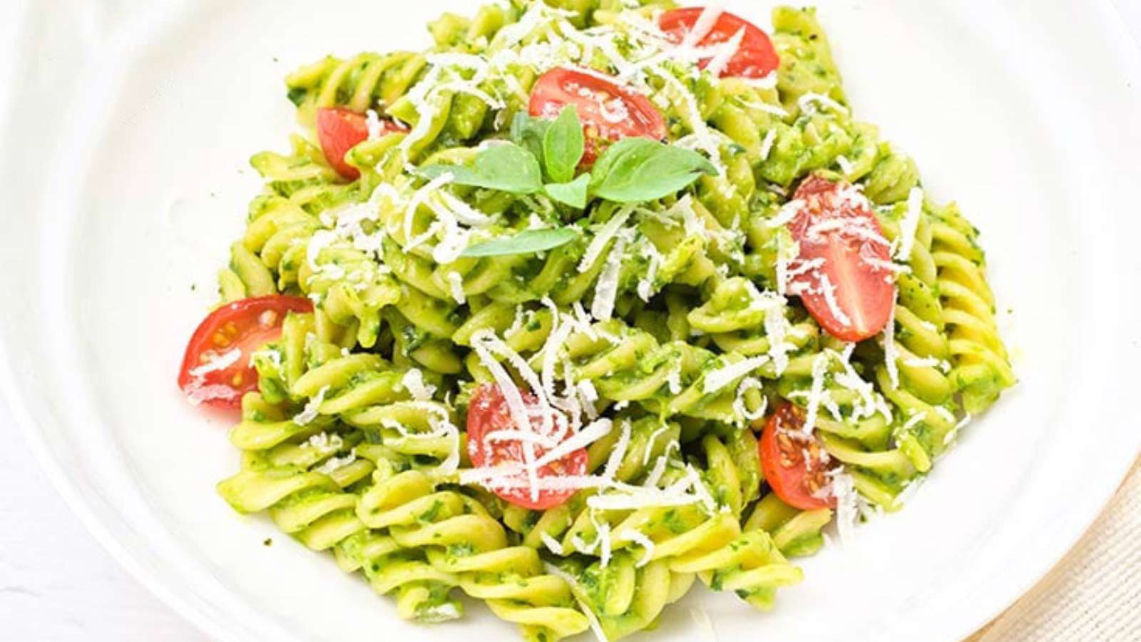 A white pasta bowl filled with Avocado Pasta, fresh grape tomatoes and grated parmesan cheese.