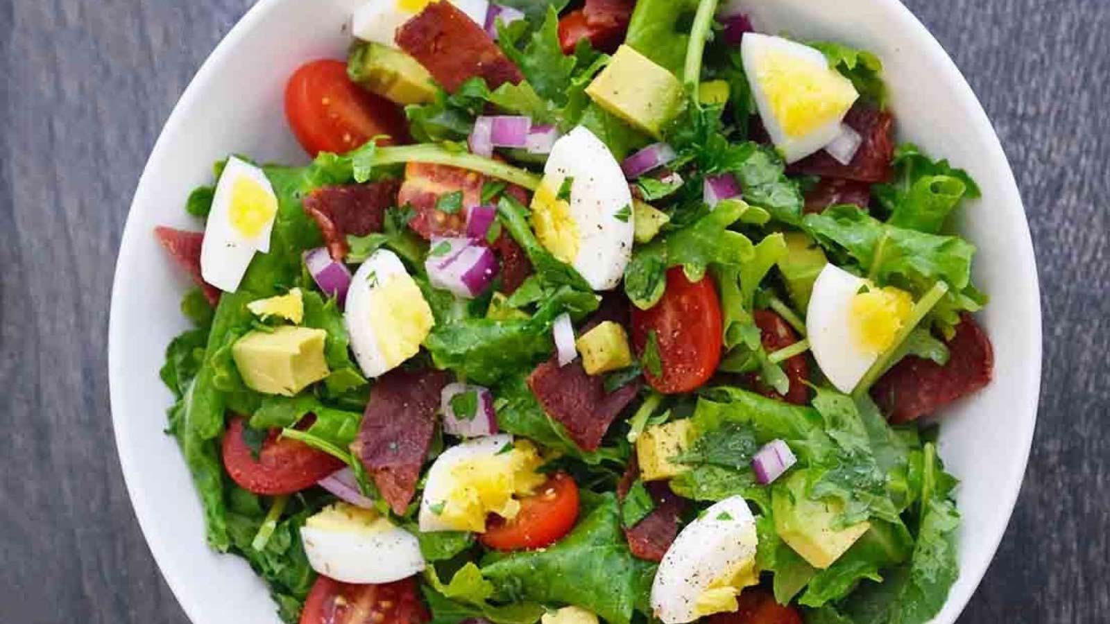 An overhead view of a white bowl filled with baby kale salad.