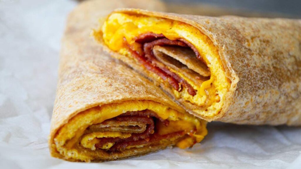 A bacon and egg wrap cut in half an laying on a piece of white parchment paper.