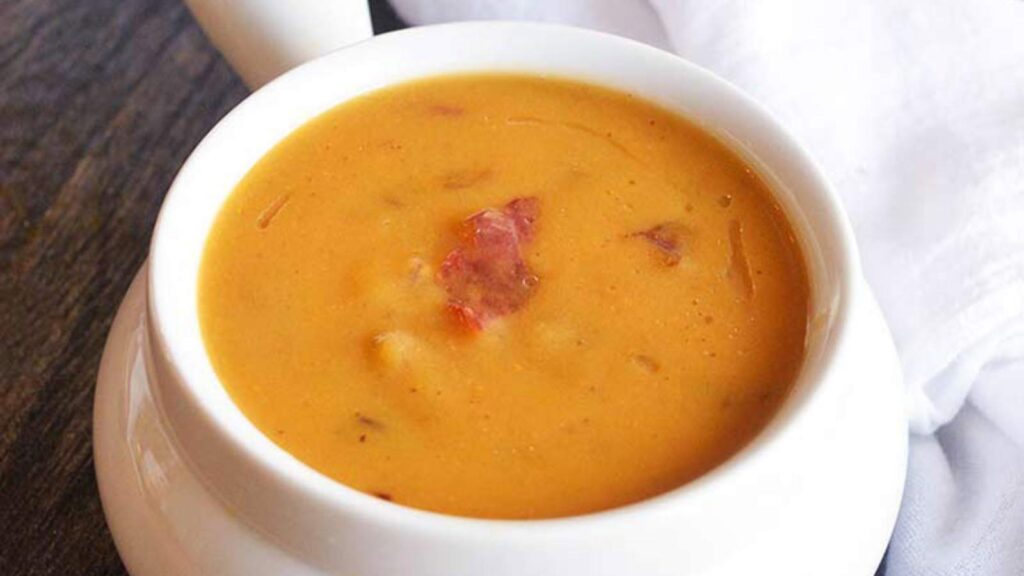 A white crock filled with Bacon Sweet Potato Soup, sitting on a table.