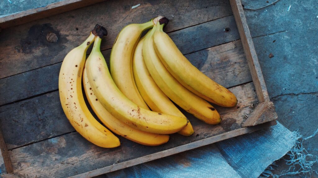 A wood tray holds two bunches of bananas with a few brown spots on them.