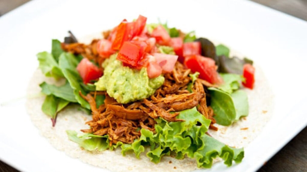Slow Cooker BBQ Chicken on a tortilla with lettuce, tomatoes and guacamole.