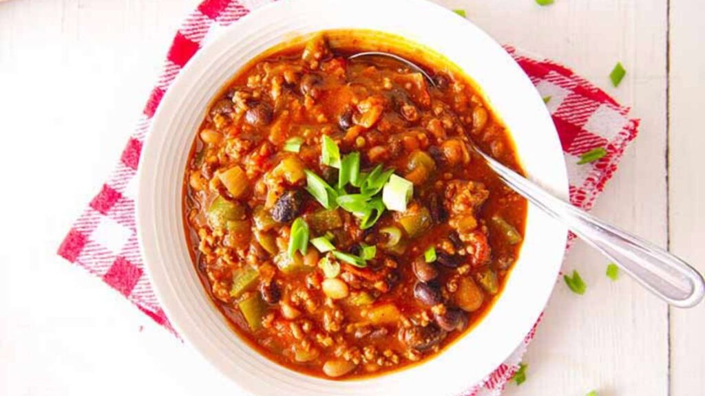 A bowl of beef chili on a table with a spoon.