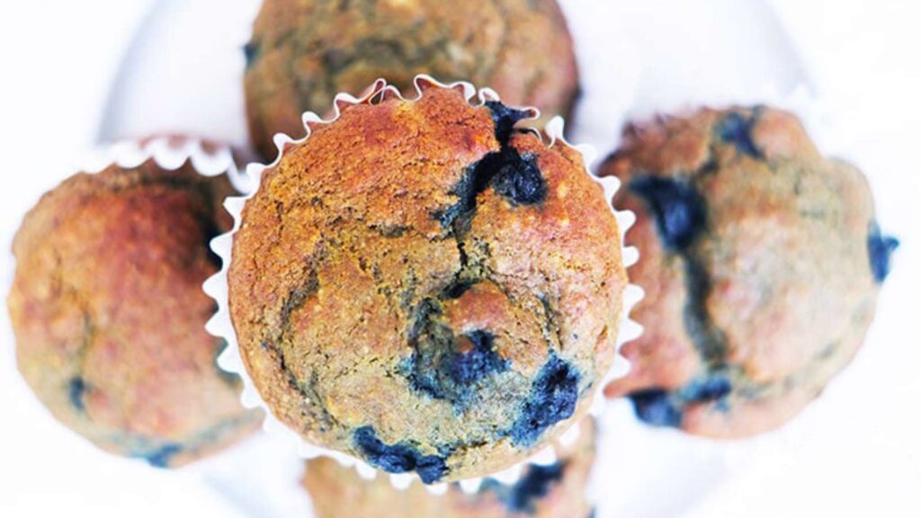 An overhead view of a pile of Blueberry Corn Muffins on a white plate.