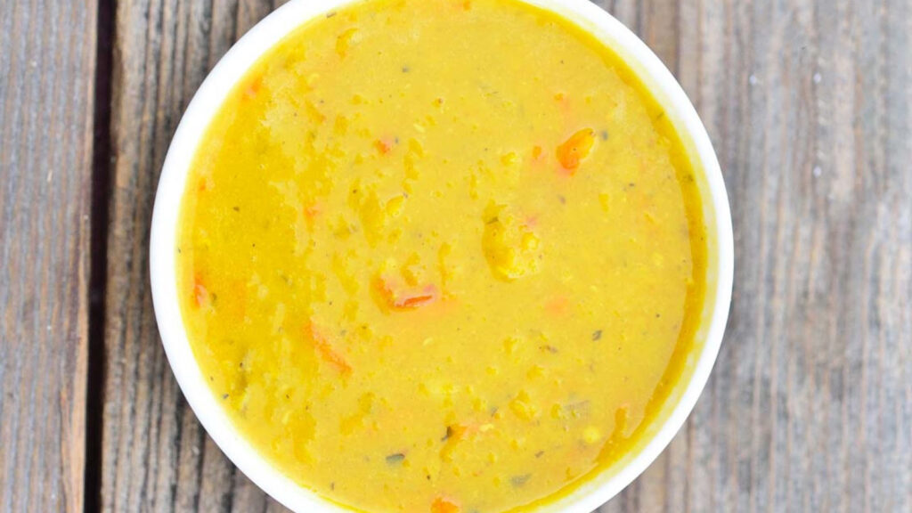 An overhead view of a white bowl filled with Carrot Ginger Lentil Soup.