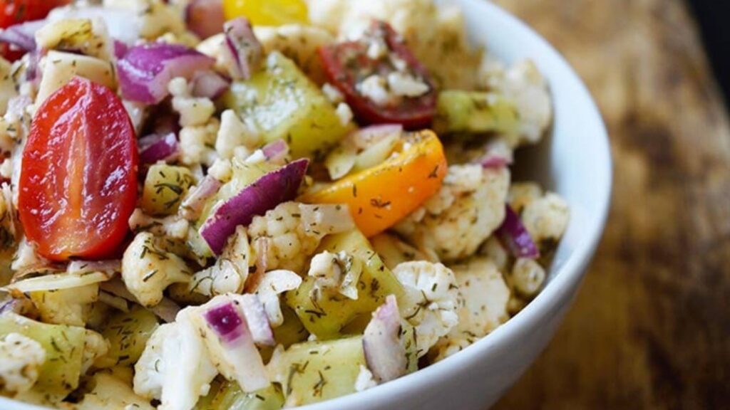 A white bowl filled with cauliflower salad sitting on a wood surface.