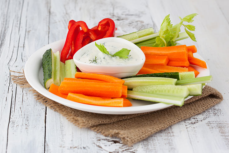 A white plate of vegetable sticks with a small white bowl of dip in the middle.