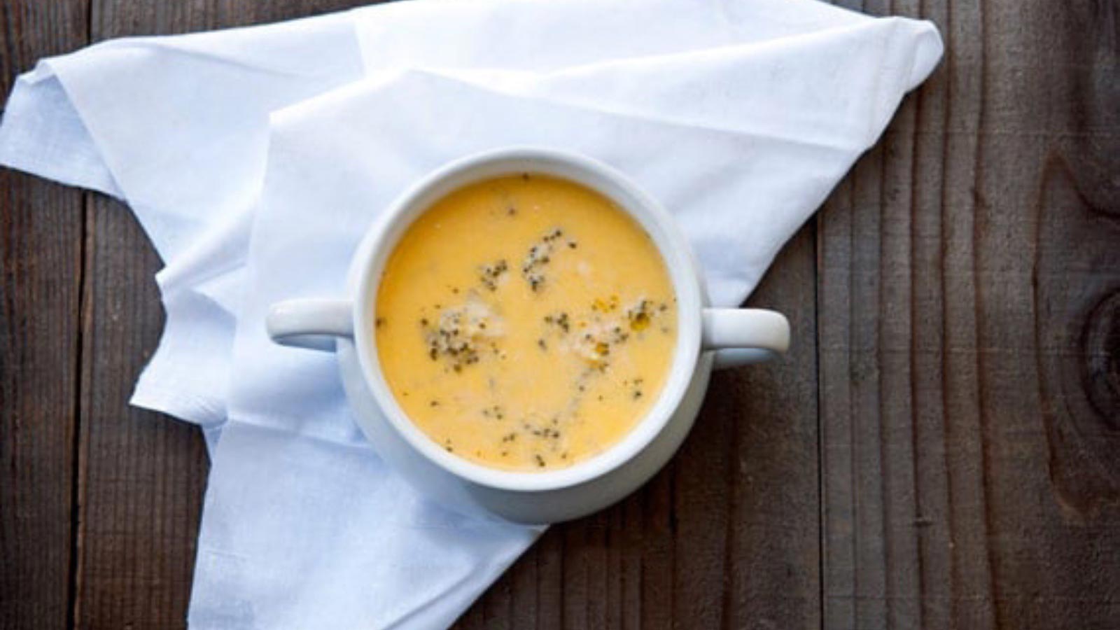 A white crock filled with cheddar broccoli soup on a wooden table.