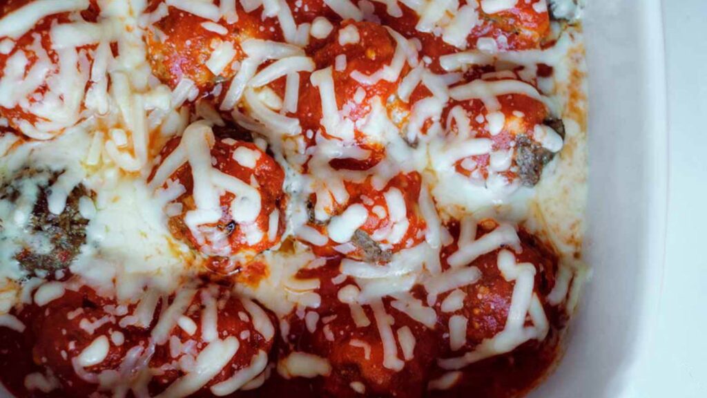 Overhead view looking down into a white casserole dish filled with this Cheesy Baked Meatballs Recipe.