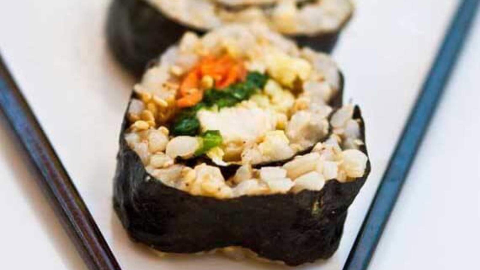 Chicken Sushi lined up on a white plate with black chopsticks.
