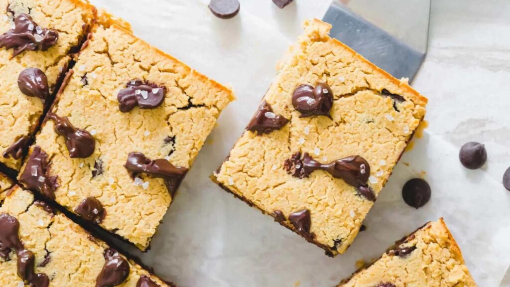 An overhead view of just-cut chickpea blondies with one being picked up by a metal spatula.