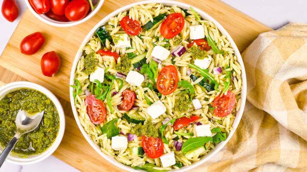 An overhead view of a white bowl filled with orzo pasta with pesto sacue.
