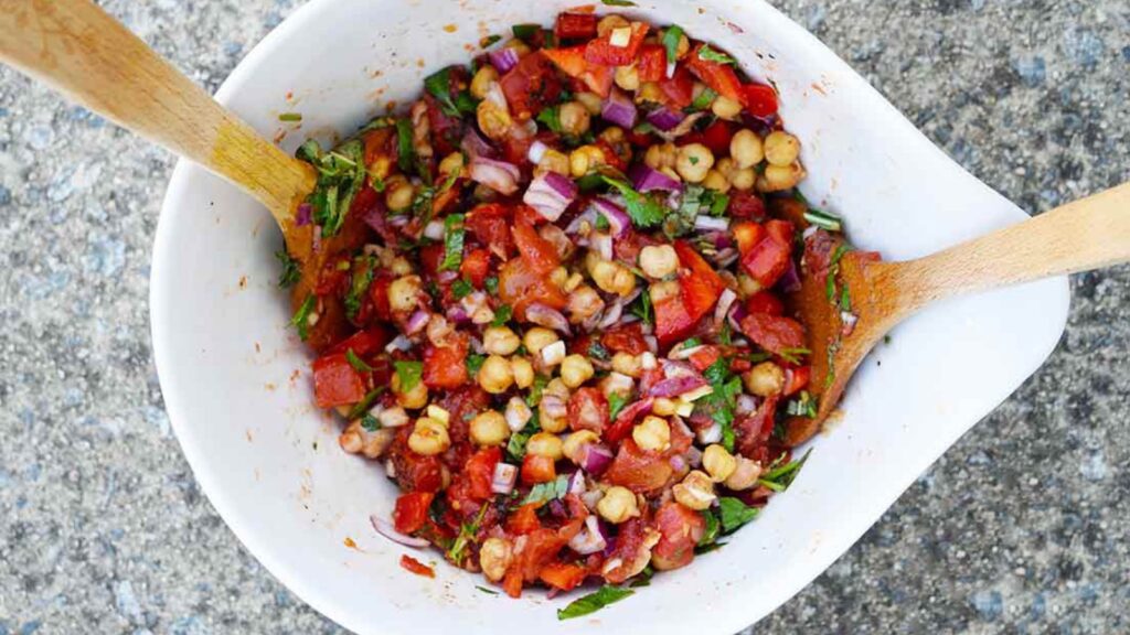 A large white mixing bowl with tongs in it sits halfway filled with chickpea salad.