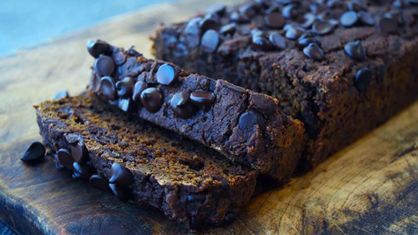 A loaf of Chocolate Pumpkin Bread on a cutting boar with two slices cut from the front end.