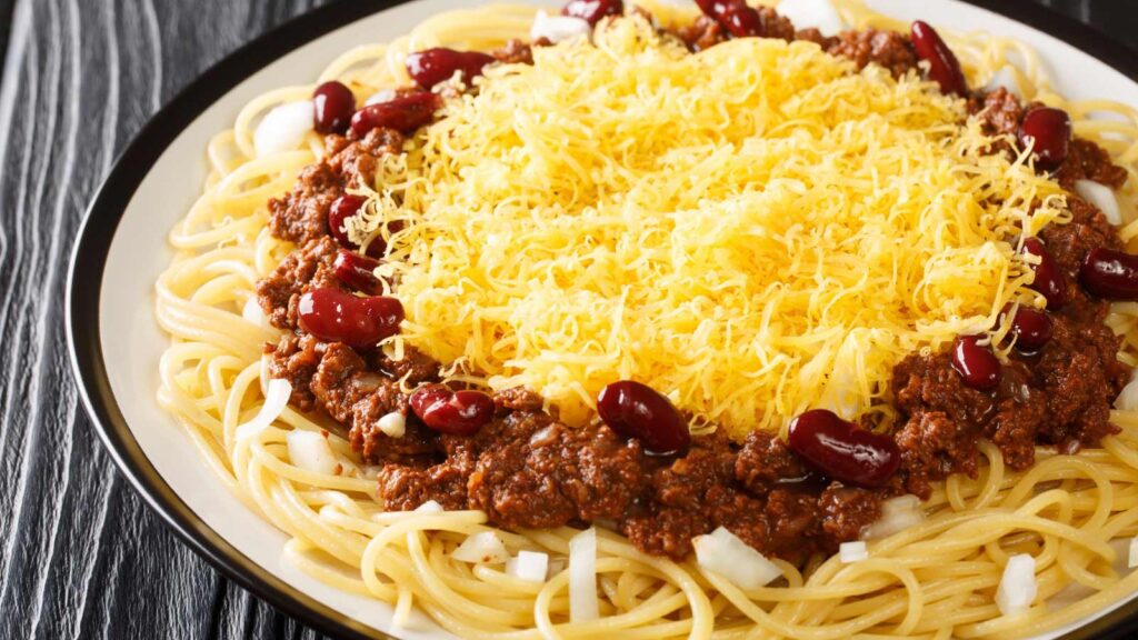 A plate of Cincinnati chili served over pasta and topped with grated cheese.