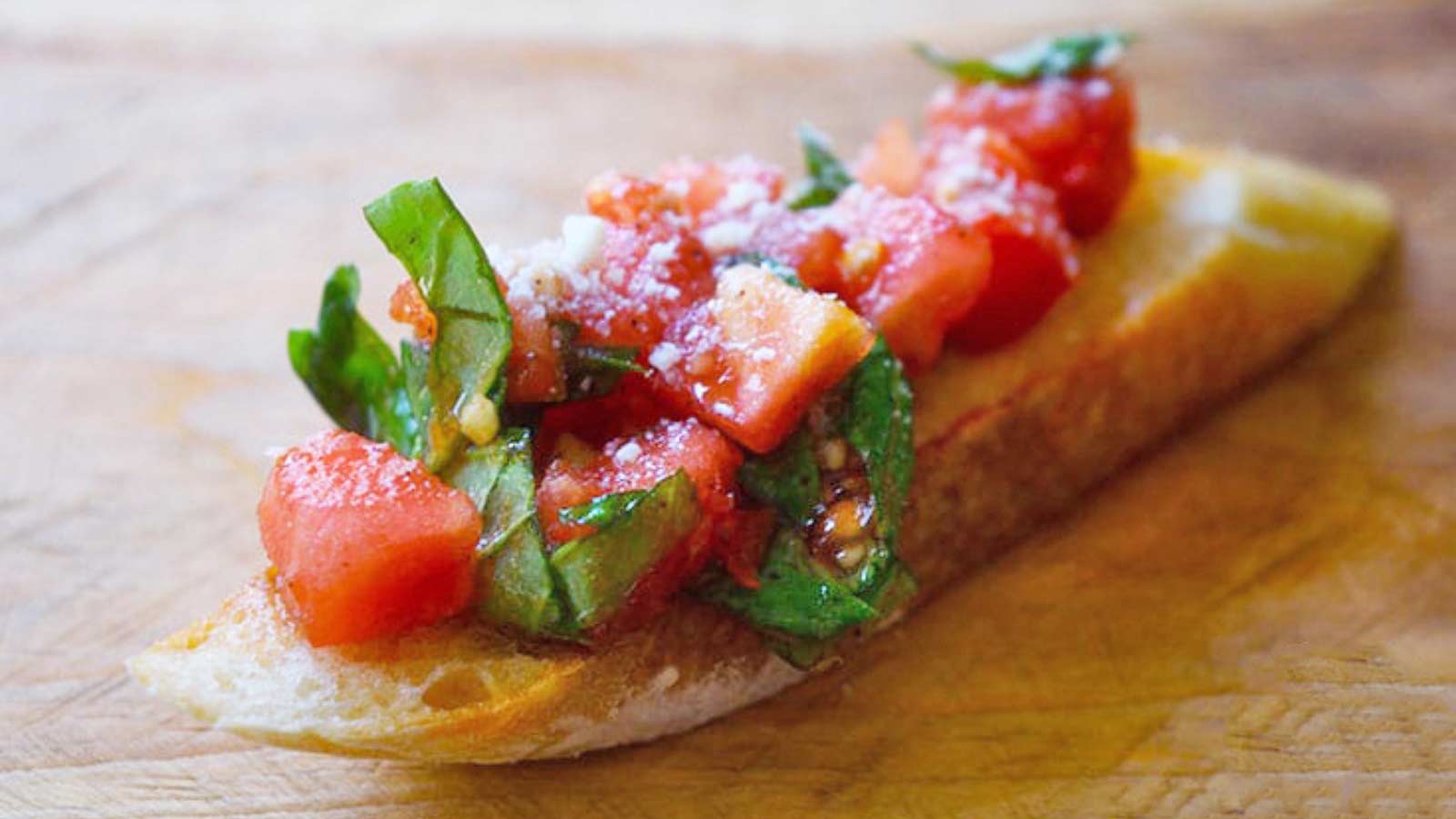 A single bruschetta on a wood cutting board.