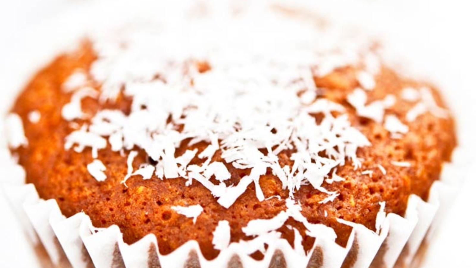 A closeup of a muffin in white paper topped with white coconut shreds.
