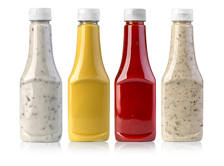 Condiments in glass bottles on white background.