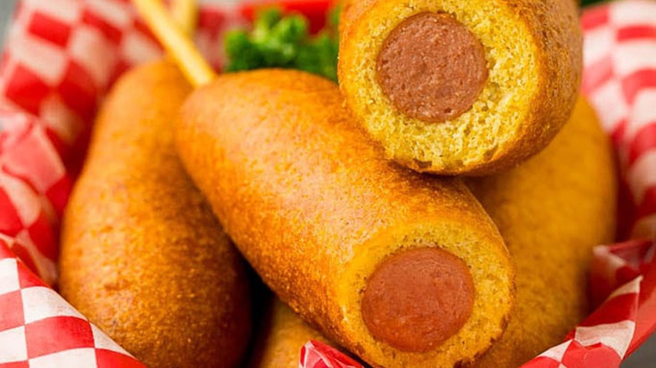 An upclose view of corn dogs in a food basket. Two have been cut open to show the hot dog inside.