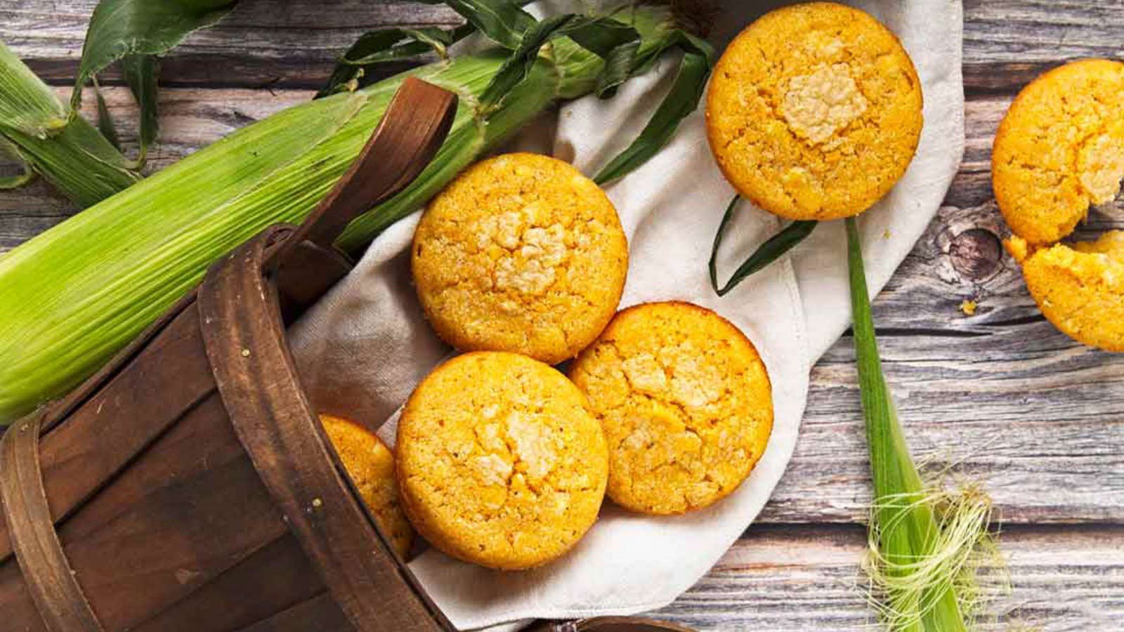 A basket on its side with cornbread muffins coming out of it onto a wood table.