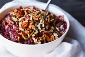 A large, white bowl of cranberry oatmeal topped with chopped pecans.