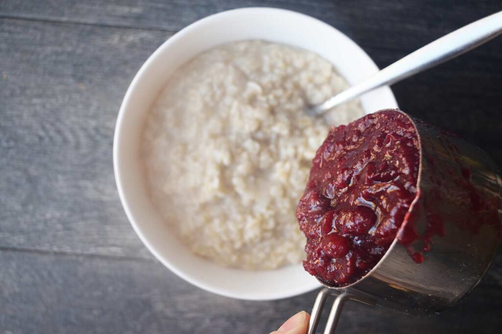 Adding cranberry sauce to a bowl of plain oatmeal.