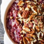 An overhead partial view of a white bowl filled with Cranberry Oatmeal and garnished with pecans.