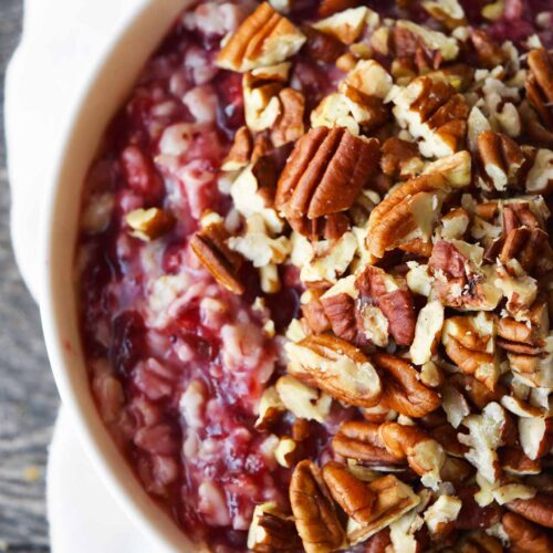 An overhead partial view of a white bowl filled with Cranberry Oatmeal and garnished with pecans.