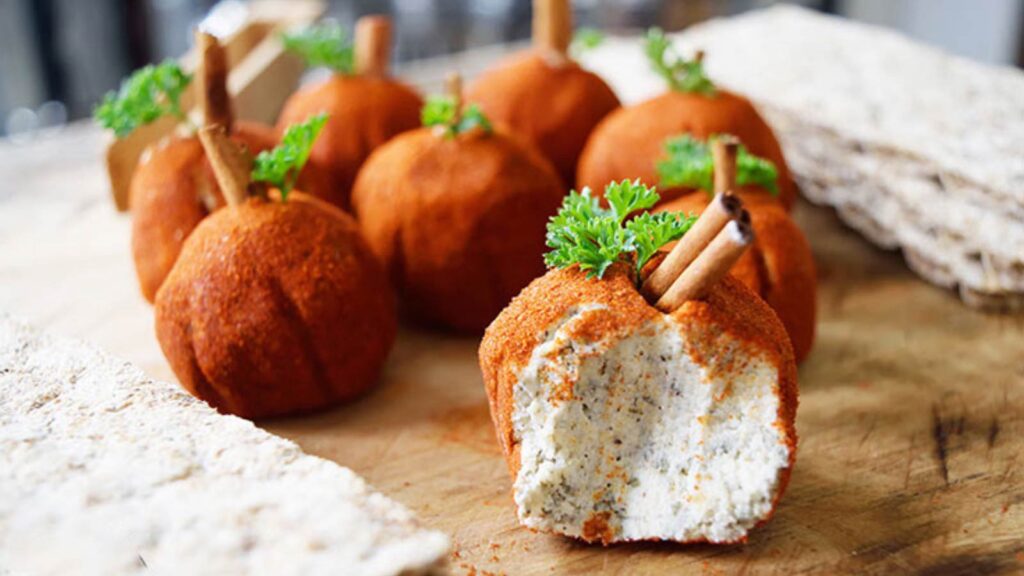 A cutting board with eight small, pumpkin-shaped, cream cheese balls and some crackers.