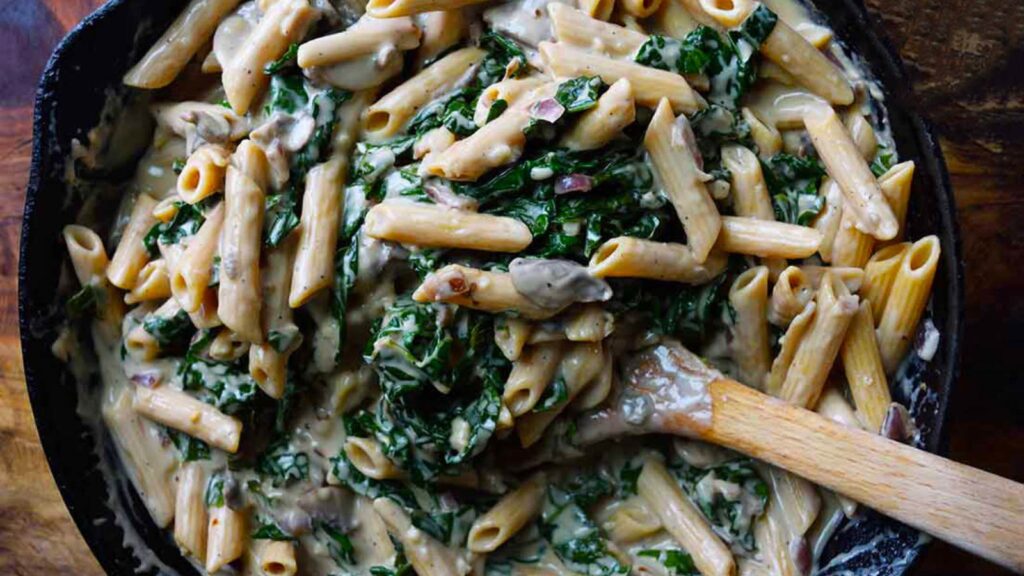 An overhead view looking down into a cast iron skillet filled with Creamy Kale And Mushroom Pasta.