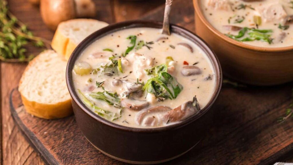 A bowl of creamy mushroom kale turkey soup in a brown bowl.