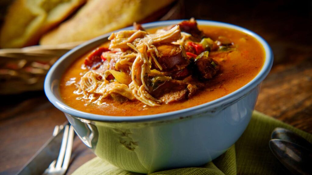 A blue bowl filled with Creole chicken stew sits on a table.