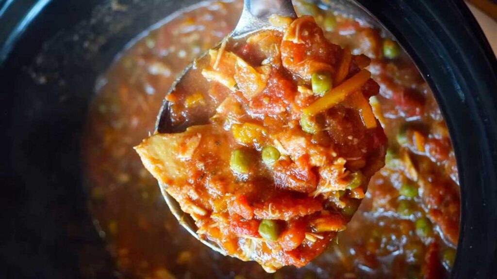 An overhead view of a ladle lifting out some crockpot Italian chicken from a slow cooker crock.