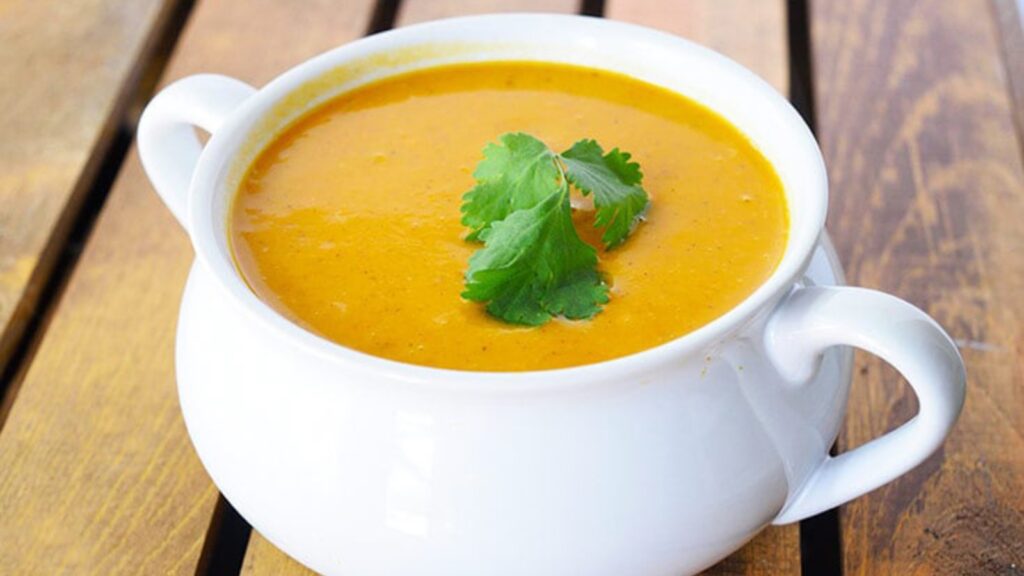 A white crock filled with curried sweet potato soup on a table.