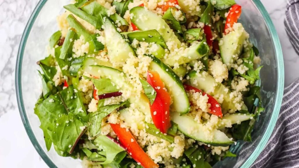 A clear, glass bowl filled with dandelion greens couscous salad.