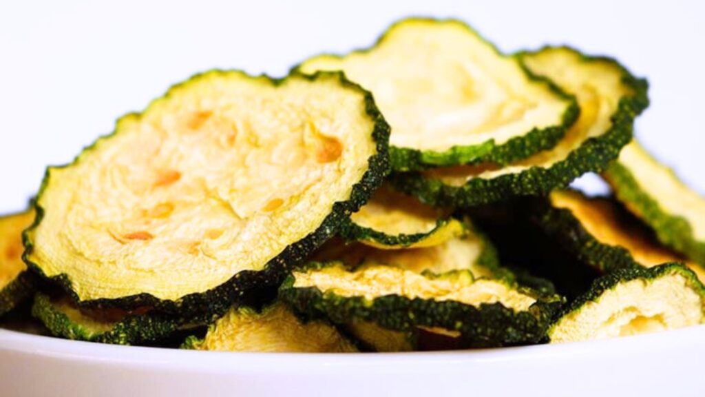 A white bowl on a white background, filled with dehydrated zucchini chips.