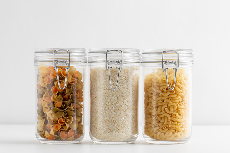Dry pasta and rice in three glass jars on a white background.