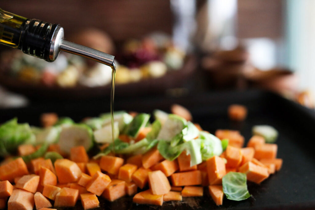 Pouring oil over vegetables on a sheet pan.