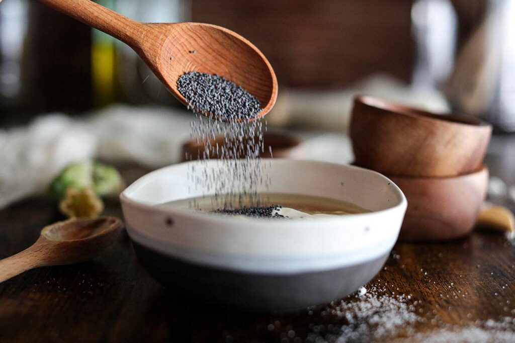 Adding poppy seeds to a small bowl of dressing.