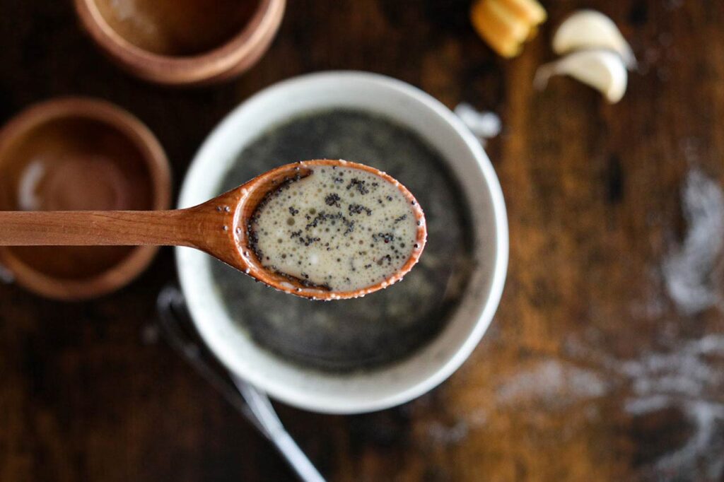 A wooden spoon lifts up some dressing out of a bowl.