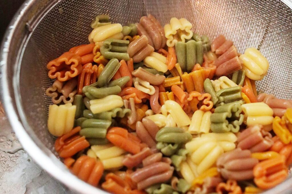 Pasta being rinsed in a fine mesh sieve after cooking.