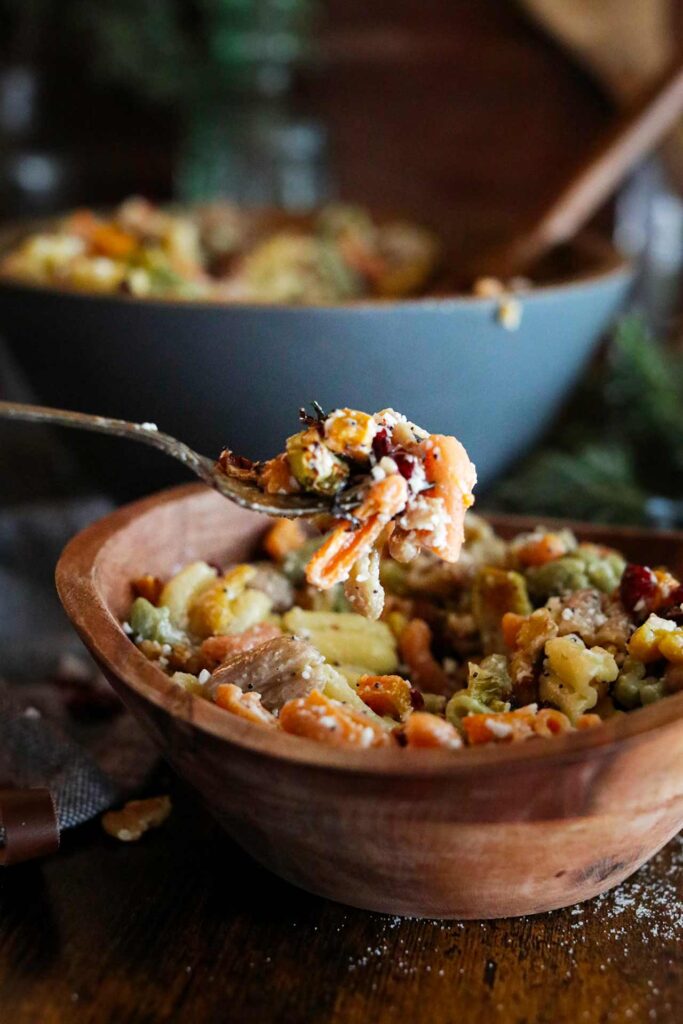 A side view of a fork lifting a bite of Fall Harvest Pasta Salad out of a wooden bowl.