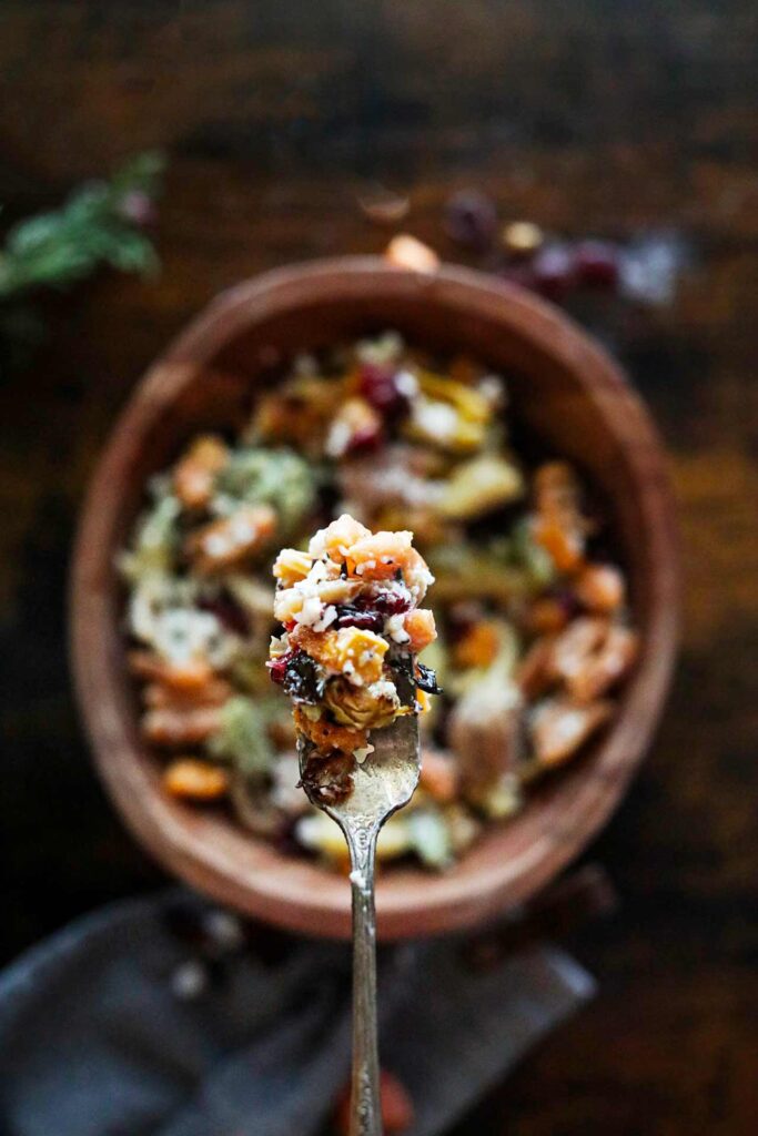 A fork lifts a bite of fall harvest pasta salad out of a wooden bowl.