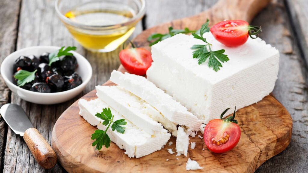 A cutting board with a sliced block of feta cheese garnished with halved grape tomatoes.