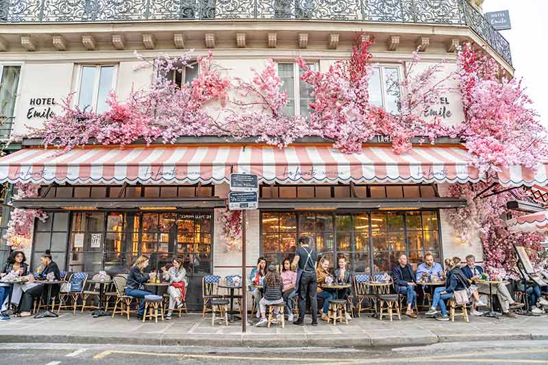 People enjoy dining at a traditional cafe in Paris, with flowery, spring decor.