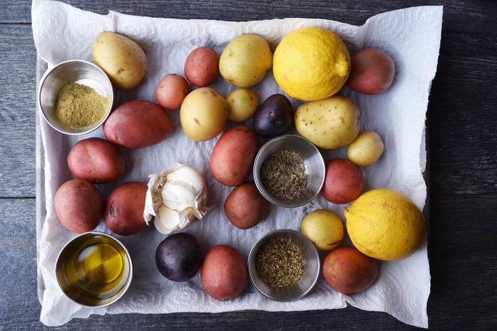 Garlic Lemon Potatoes Recipe ingredients on a paper towel-lined baking sheet. Potatoes, lemons, garlic, spices, and oil.