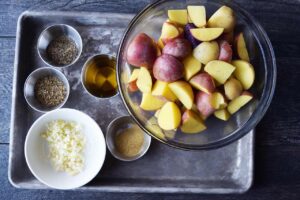 Garlic Lemon Potatoes Recipe ingredients, prepped and ready to be mixed. They sit on a metal sheet pan in individual bowls.