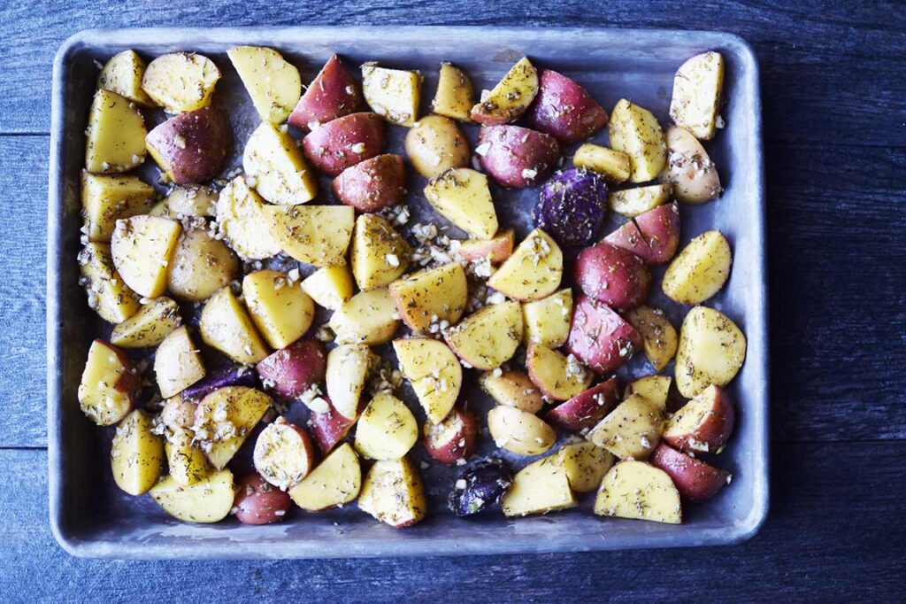 Seasoned potatoes spread out on a sheet pan.