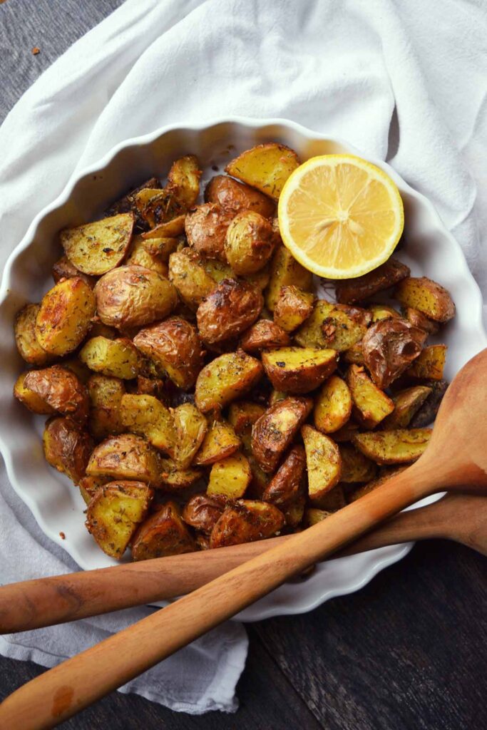 An overhead view of a white dish filled with Garlic Lemon Potatoes. A half lemon is wedged into the side of the dish.